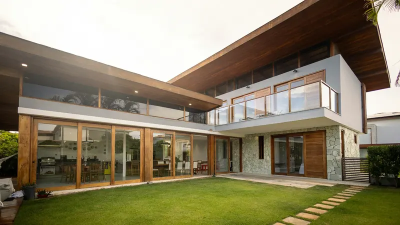 A modern two-story house with floor-to-ceiling glass, wood and stone, over a green lawn